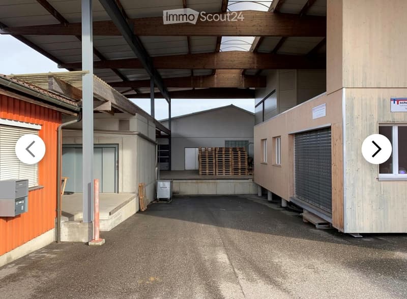 Outdoor area with multiple modular buildings, including a wooden structure with a garage door, a grey container, and an orange building with a raised ground floor.