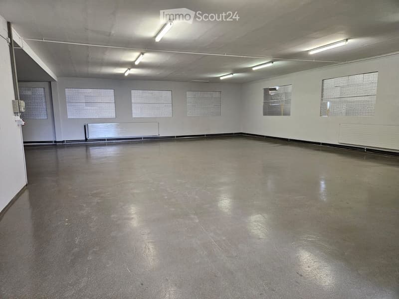 Empty room with bare walls, concrete floor, and large windows with metal grilles. No furniture or equipment present.