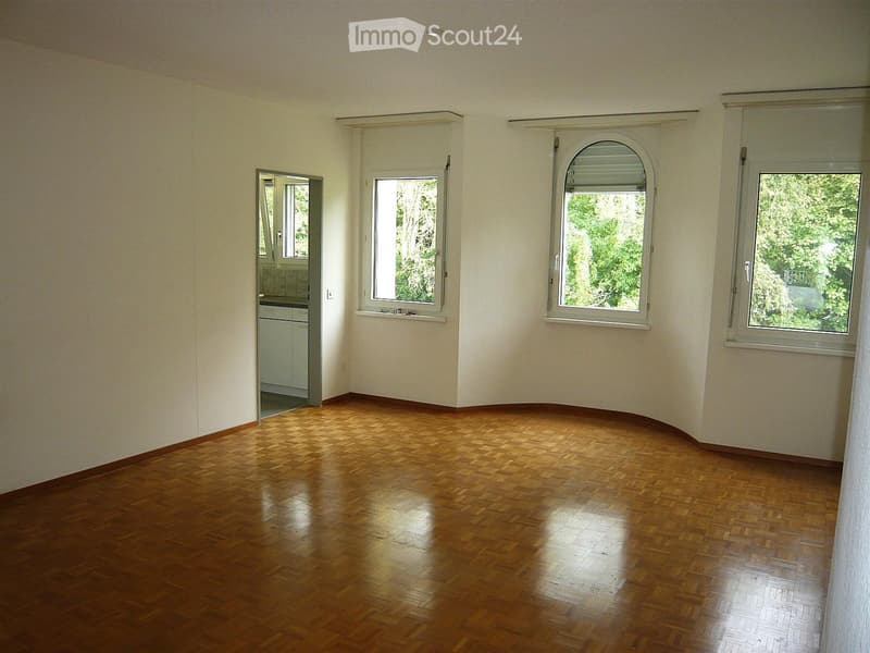 Empty room with wooden flooring, large windows, and a doorway leading to another room.