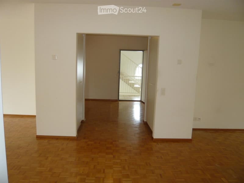 Empty hallway with wooden flooring and white walls, featuring a doorway leading to another room.