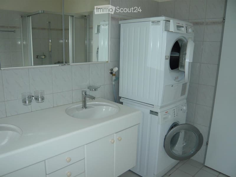 Bathroom with a white sink, faucet, mirror, two cups, bathtub, and a stacked washing machine and dryer unit.