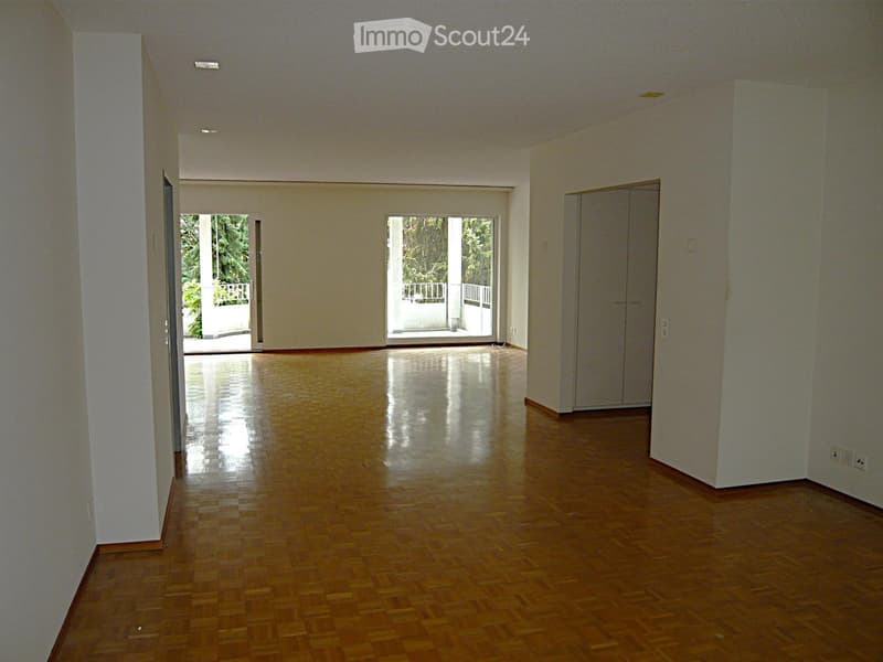 Empty room with wooden flooring, white walls, and large windows leading to a balcony area.