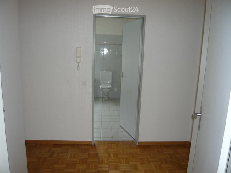 Empty room with wooden flooring and a partially open door leading to a small bathroom with a toilet and tiled walls.