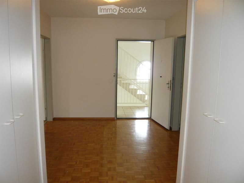 Empty hallway with wooden flooring, white walls, and a glass door leading to a balcony area.