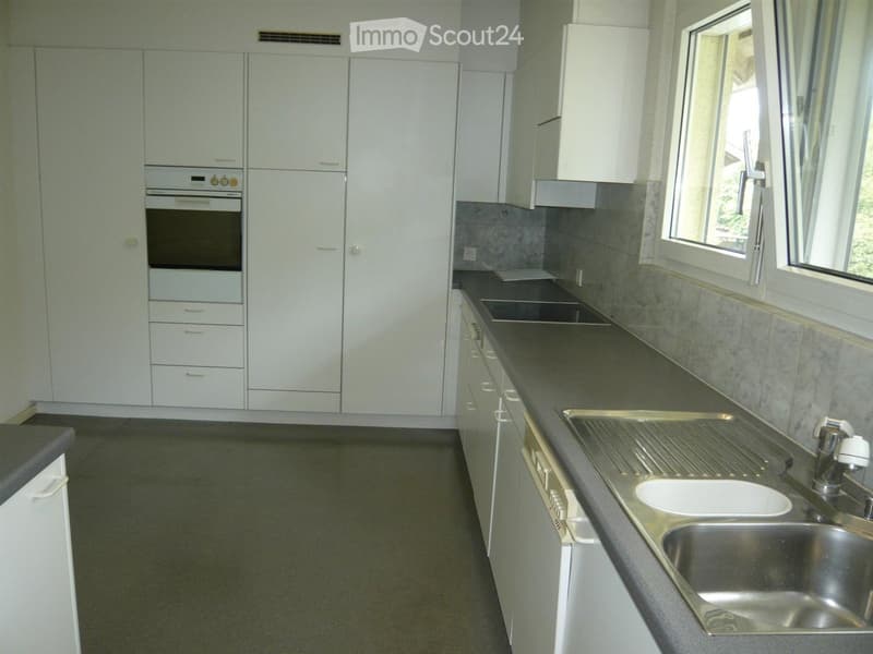 Modern kitchen with white cabinets, stainless steel sink, and built-in oven. Countertops are dark grey, and the floor is a dark grey tile.