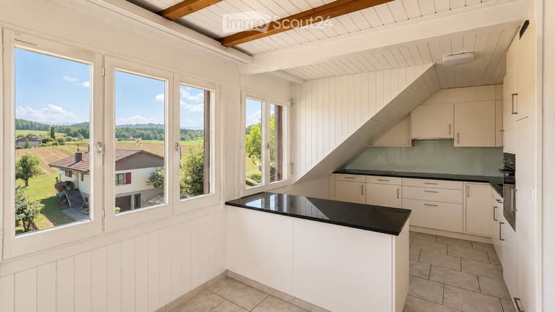 Bright, modern kitchen with white cabinets, black countertop, and large windows overlooking a scenic countryside view.