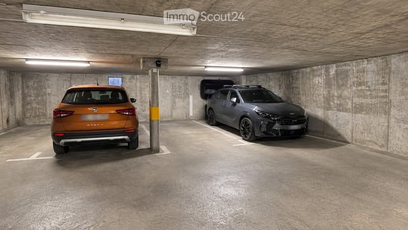 Underground parking area with two parked cars, concrete walls, and ceiling lights.