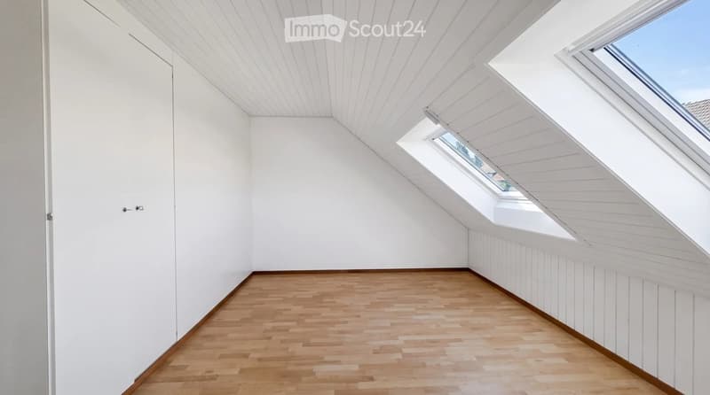 Empty attic room with wooden flooring, white walls, and skylight windows.