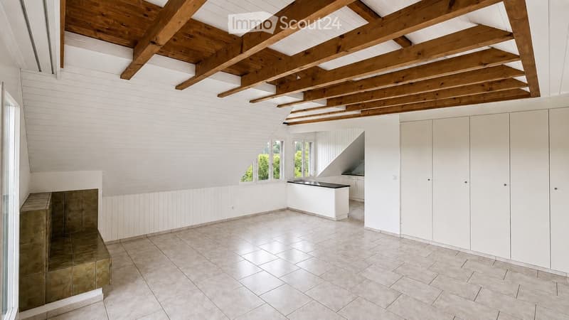 Bright, airy room with exposed wooden beams, white walls, and a kitchen island with black countertop. Large windows provide natural light, and built-in cabinets line one wall.