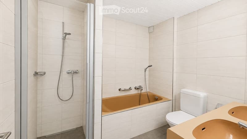 Modern bathroom with a bathtub, toilet, sink, and a separate shower area. The walls are tiled in light beige, and the fixtures are sleek and contemporary.