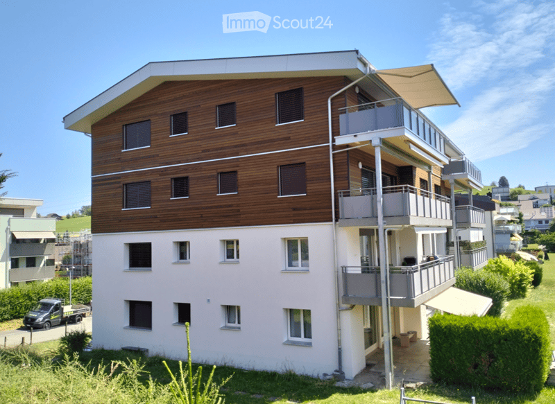 Modern two-story residential building with a combination of wooden and light-colored facades, multiple balconies, and contemporary design.