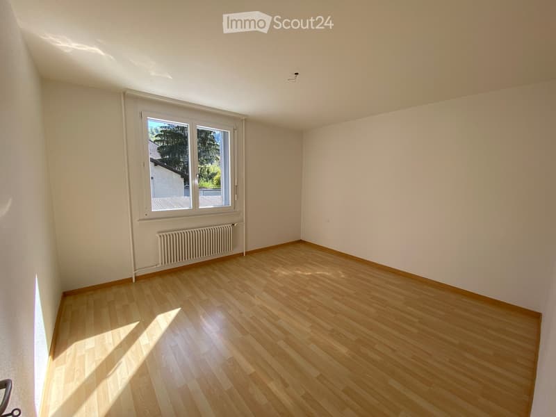 Empty room with wooden flooring, white walls, and a window with a radiator below it.