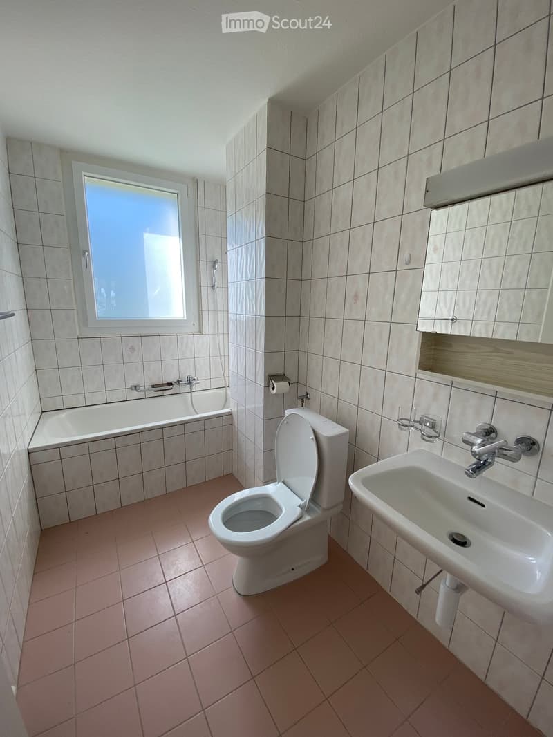 Bathroom with tiled walls and floor, featuring a toilet, sink, bathtub, and window providing natural light.
