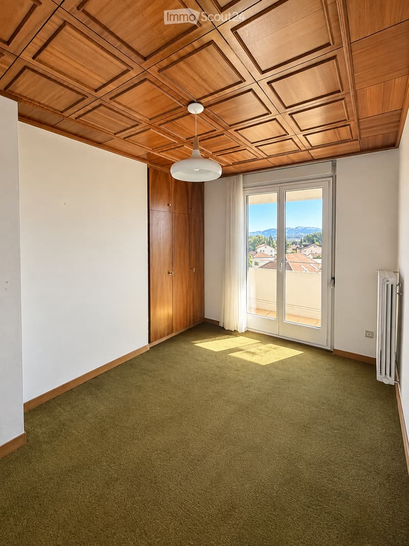 Empty room with green carpet, white walls, wooden ceiling, and large sliding glass doors leading to a balcony with a scenic view.