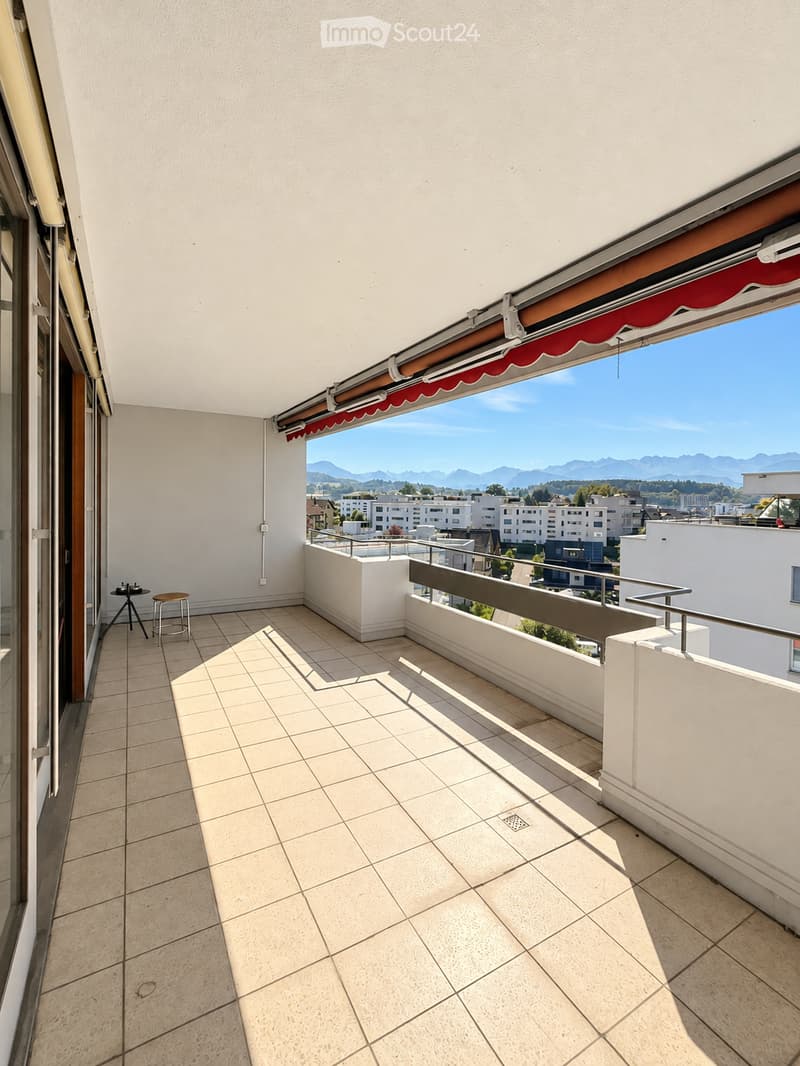 Balcony with tiled floor, white walls, metal railing, and a retractable awning. Offers a scenic view of the city and mountains.
