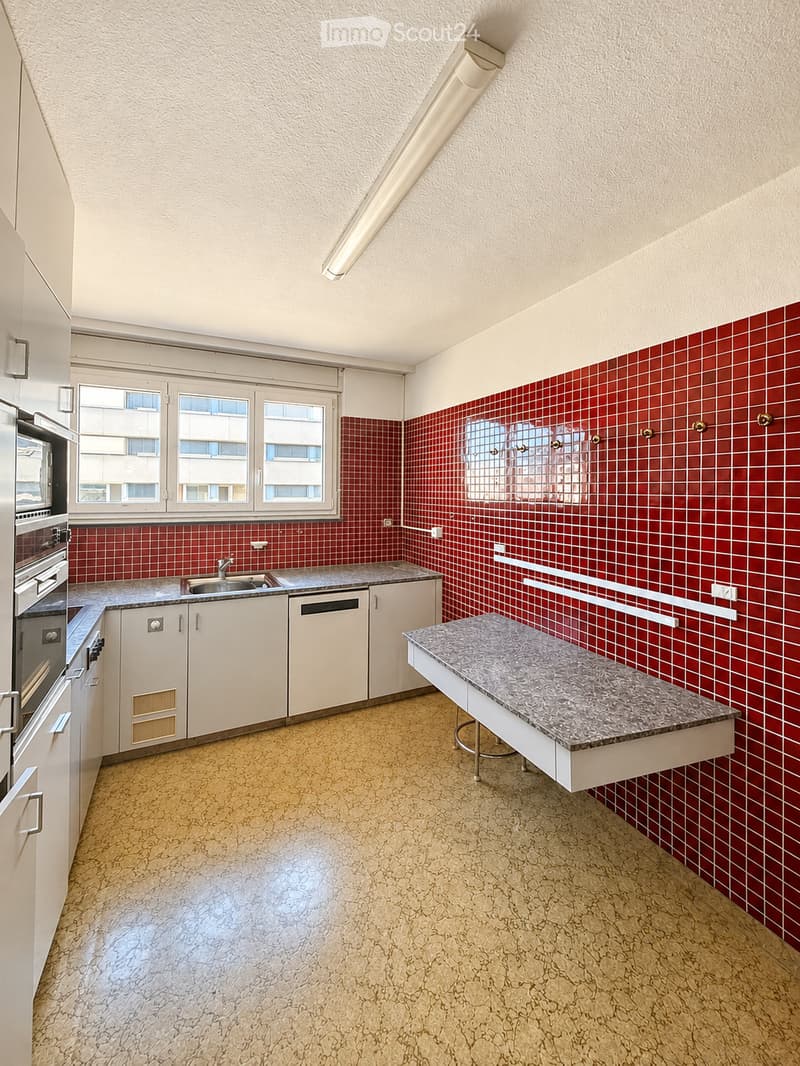 Empty kitchen with white cabinets, red tiled backsplash, granite countertop, sink, oven, and dishwasher. Natural light from windows.