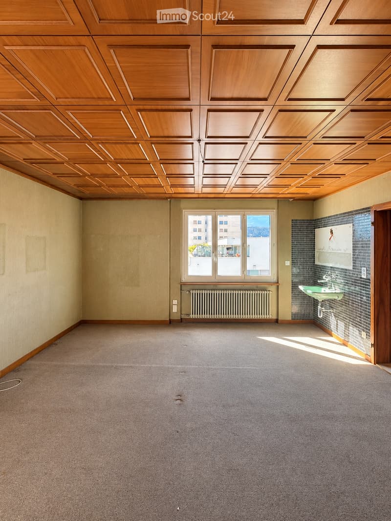 Empty room with wooden paneled ceiling, carpeted floor, large windows, radiator, and a small sink in the corner.