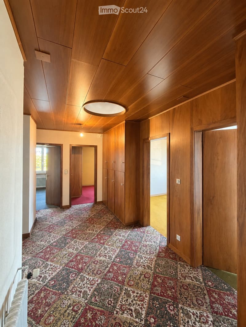Wooden-paneled hallway with patterned carpet, multiple doors, and recessed lighting.