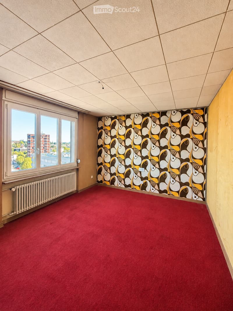 Empty room with red carpet, beige walls, large windows, radiator, and decorative wall mural.