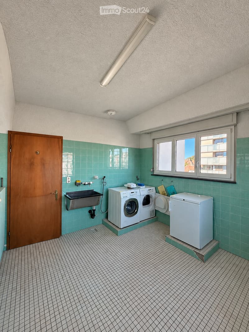 Laundry room with green tiled walls, white tiled floor, and a window. Contains a washing machine, dryer, and sink.