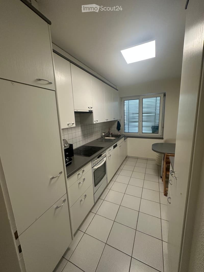 Modern kitchen with white cabinets, tiled floor, and a small round table near the window.
