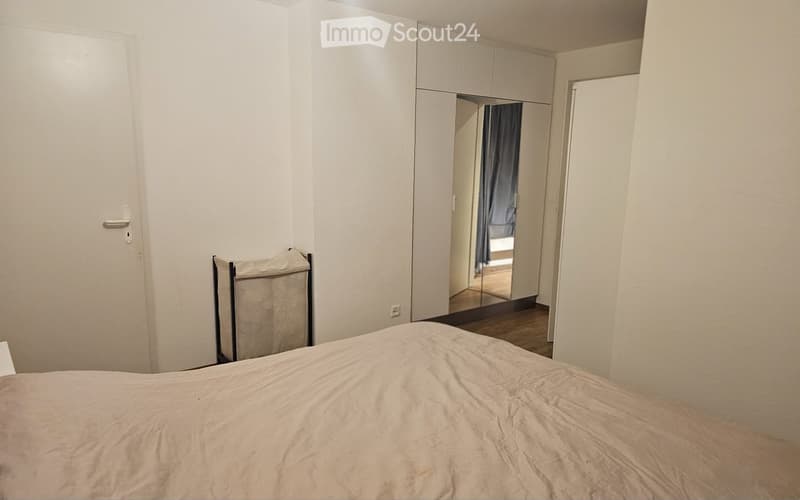 Bedroom with a neatly made bed, a large wardrobe with mirrored doors, and a curtain visible in the adjacent space.