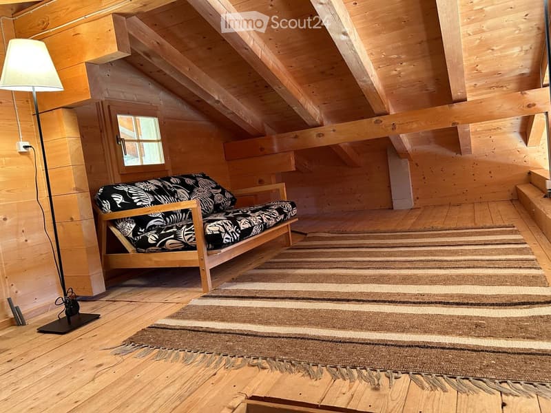 attic room with wooden beams, couch, rug, lamp, and wooden floor