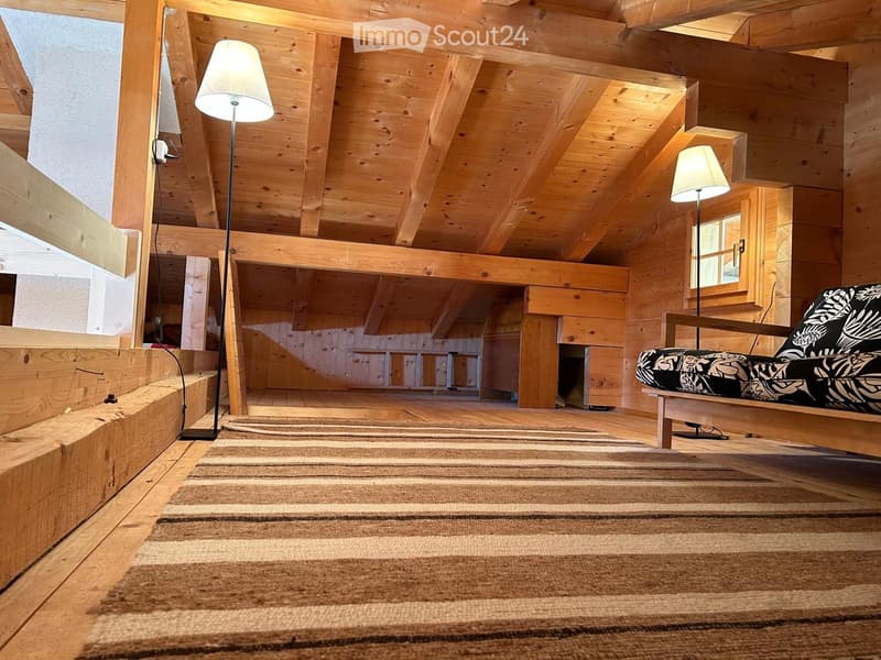 wooden attic room with wooden walls, beams, and flooring, sofa with cushions, two floor lamps, rug