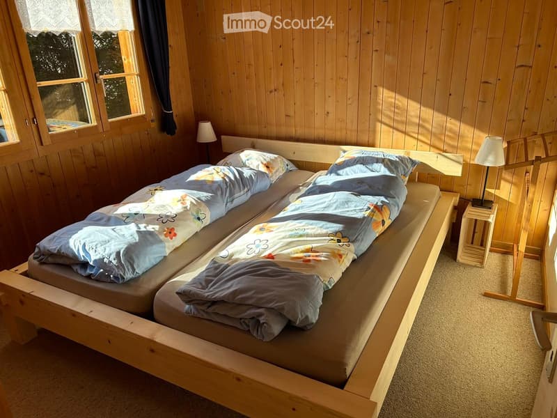 Two twin beds, wooden frame, blankets, floral pillows, lamps, wooden walls, windows with curtains