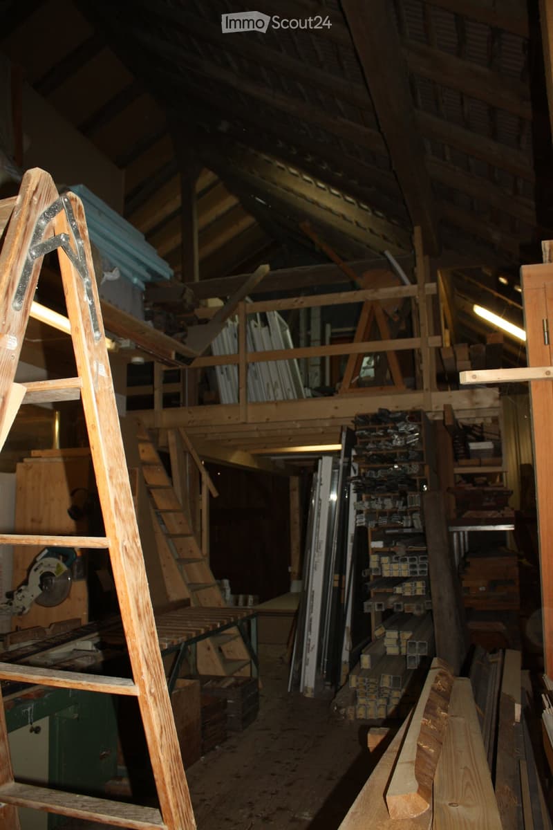 An attic or workshop space with exposed wooden beams and construction materials, including stacked lumber, metal rods, and tools.