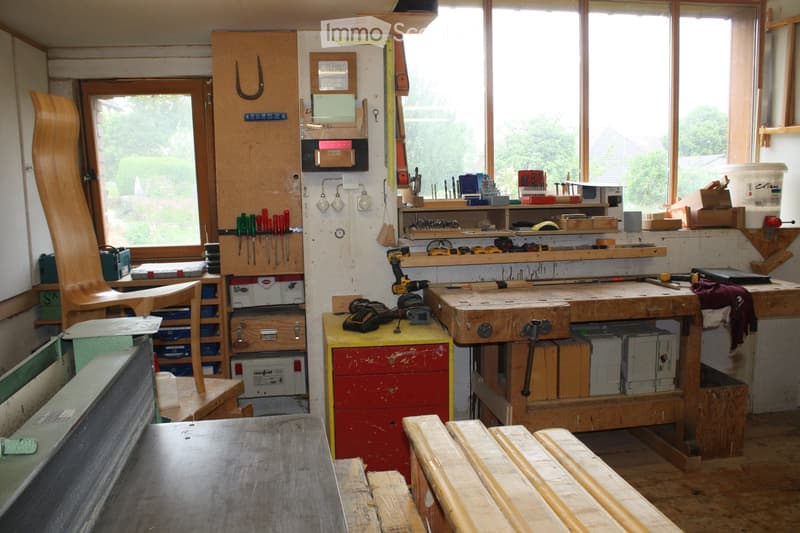 Well-lit workshop with large windows, wooden workbench, various tools, and storage cabinets.
