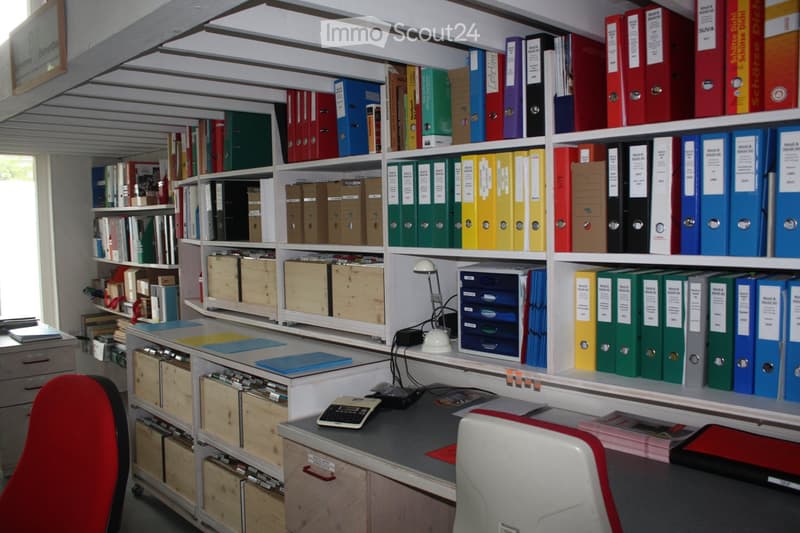 Office space with a desk, chair, shelves filled with colorful binders and books, a lamp, and a calculator on the desk.
