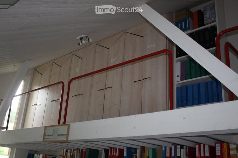 A wooden loft area with built-in cabinets and shelves filled with binders and books, featuring a white loft platform with a red metal railing and a sign on the platform.