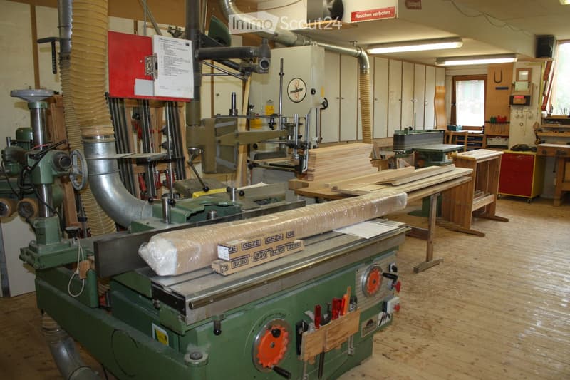 Workshop with various tools and equipment, including a saw, drill, workbench, and stacks of wood planks.