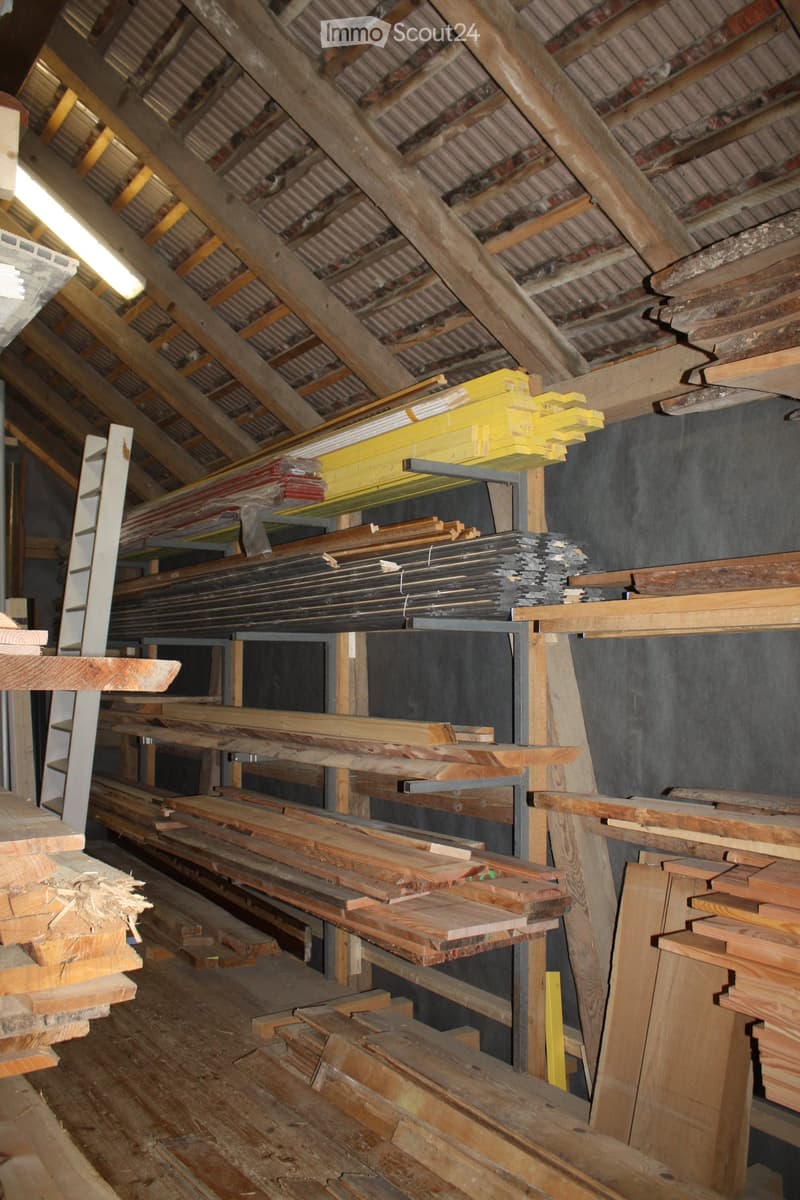 An attic space with exposed wooden beams and metal shelving holding various wooden planks and construction materials.