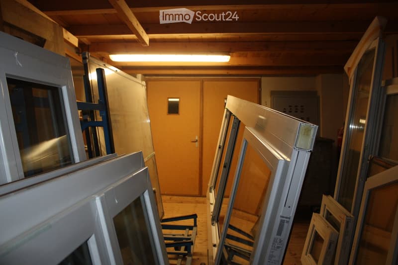 Empty room with wooden ceiling beams and flooring, featuring multiple large windows stacked against the walls, a closed wooden door, and a small electrical panel on the right side.