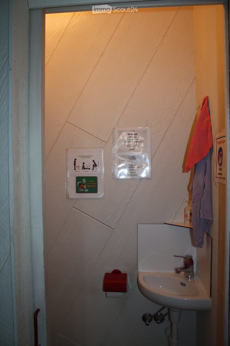 Small bathroom with a white sink, faucet, toilet paper holder, and a towel hanging on the wall. Informational posters are visible on the wall.