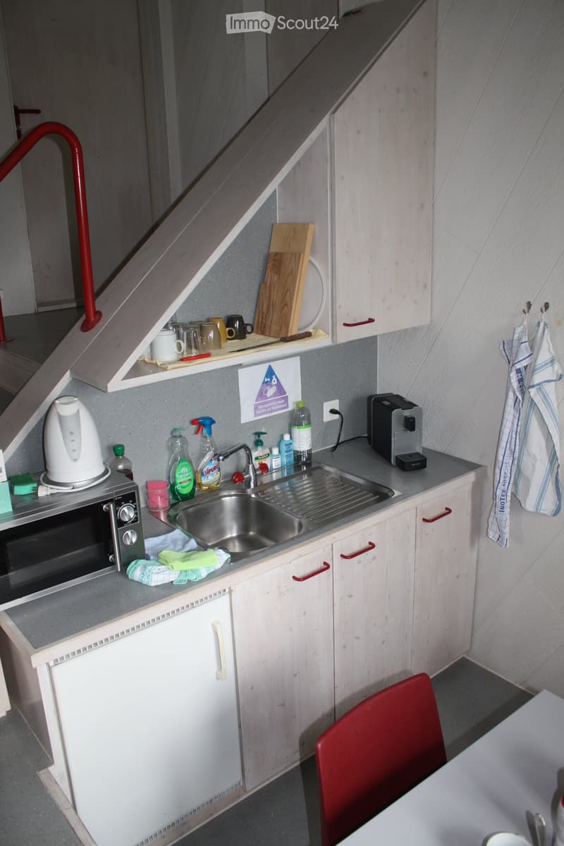 Compact kitchen with white cabinets, stainless steel sink, microwave, coffee maker, and various kitchen items on the counter.