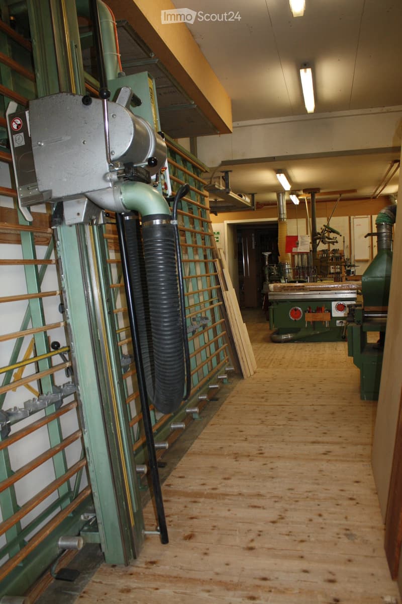 Wooden floor, green metal railing, industrial equipment, and tools in the background.