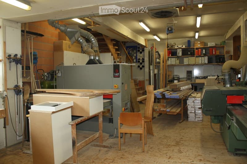 Workshop with wooden floor, shelves, machinery, and a few chairs.