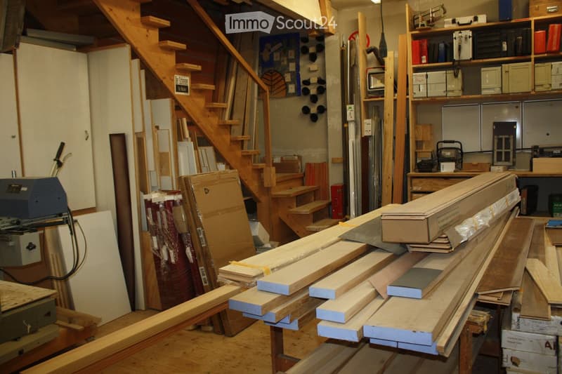 Workshop with wooden planks, tools, and shelves filled with materials and equipment.