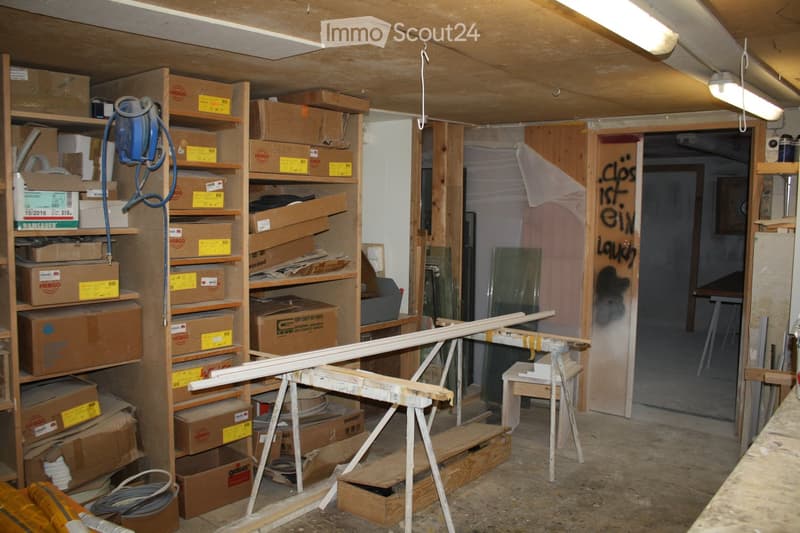 Empty storage room with exposed wooden beams, shelves filled with cardboard boxes, and construction materials scattered around.