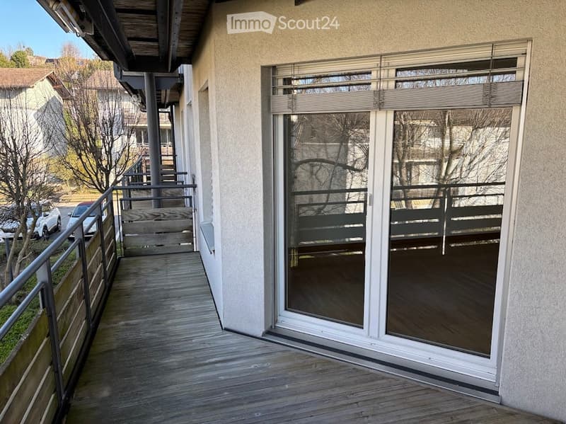 Balcony with wooden decking, metal railing, and large glass sliding doors leading to the interior.