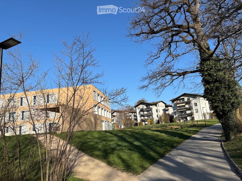 Modern residential complex with multiple buildings, surrounded by trees and a paved walkway.