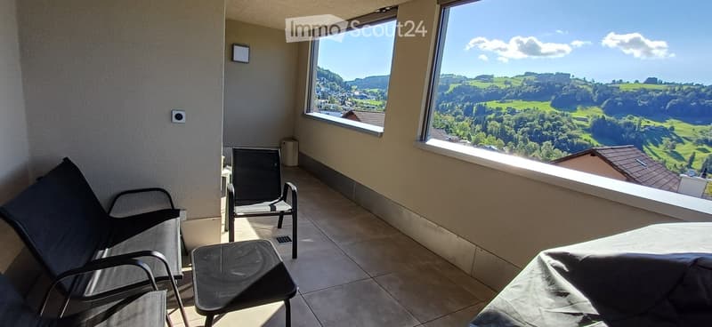 Balcony with tiled floor, two chairs, a small table, and expansive scenic view of a valley and town.