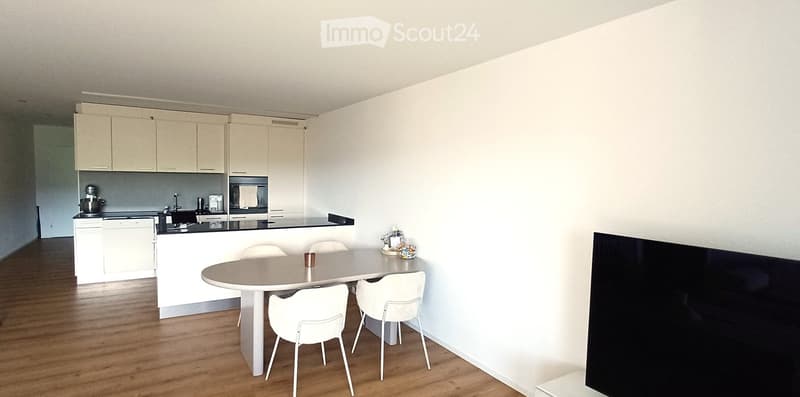 Modern kitchen with white cabinets, a round dining table with four white chairs, and a black countertop with a sink and appliances.