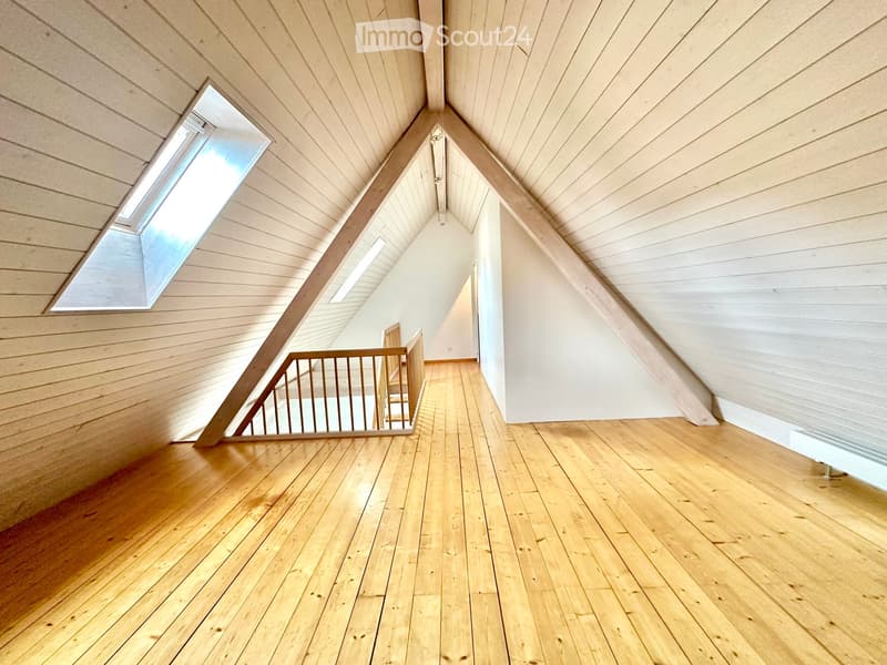 Empty attic space with wooden floors, slanted wooden ceilings, and skylights, featuring a wooden staircase leading downwards.