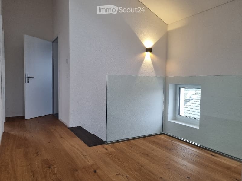 Empty room with wooden flooring, white walls, a single door, a small window, and a wall-mounted light fixture.