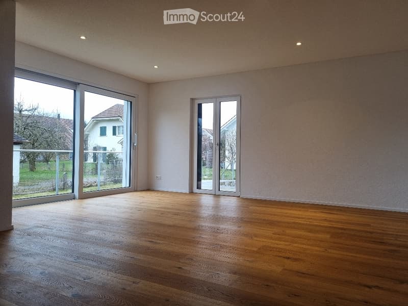 Empty room with wooden flooring, large sliding glass doors, and neutral-colored walls.