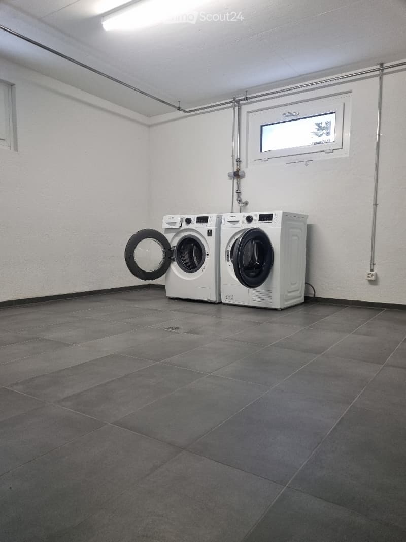 Empty room with tiled floor, white walls, and two washing machines placed against the wall.